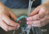 A close up of a jade bangle washed under running water by a sink.