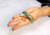 A women's hand on the white background with a jade bangle fitted partially through her hand.