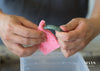 A closeup of a person hands cleaning a jade bangle with a pink sponge.